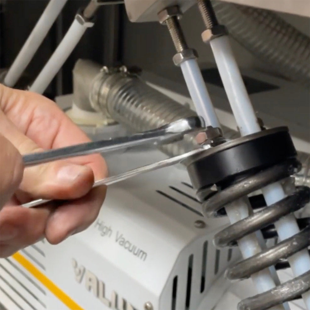 Using two wrenches to loosen the top nut on the Vac610 lid spring.